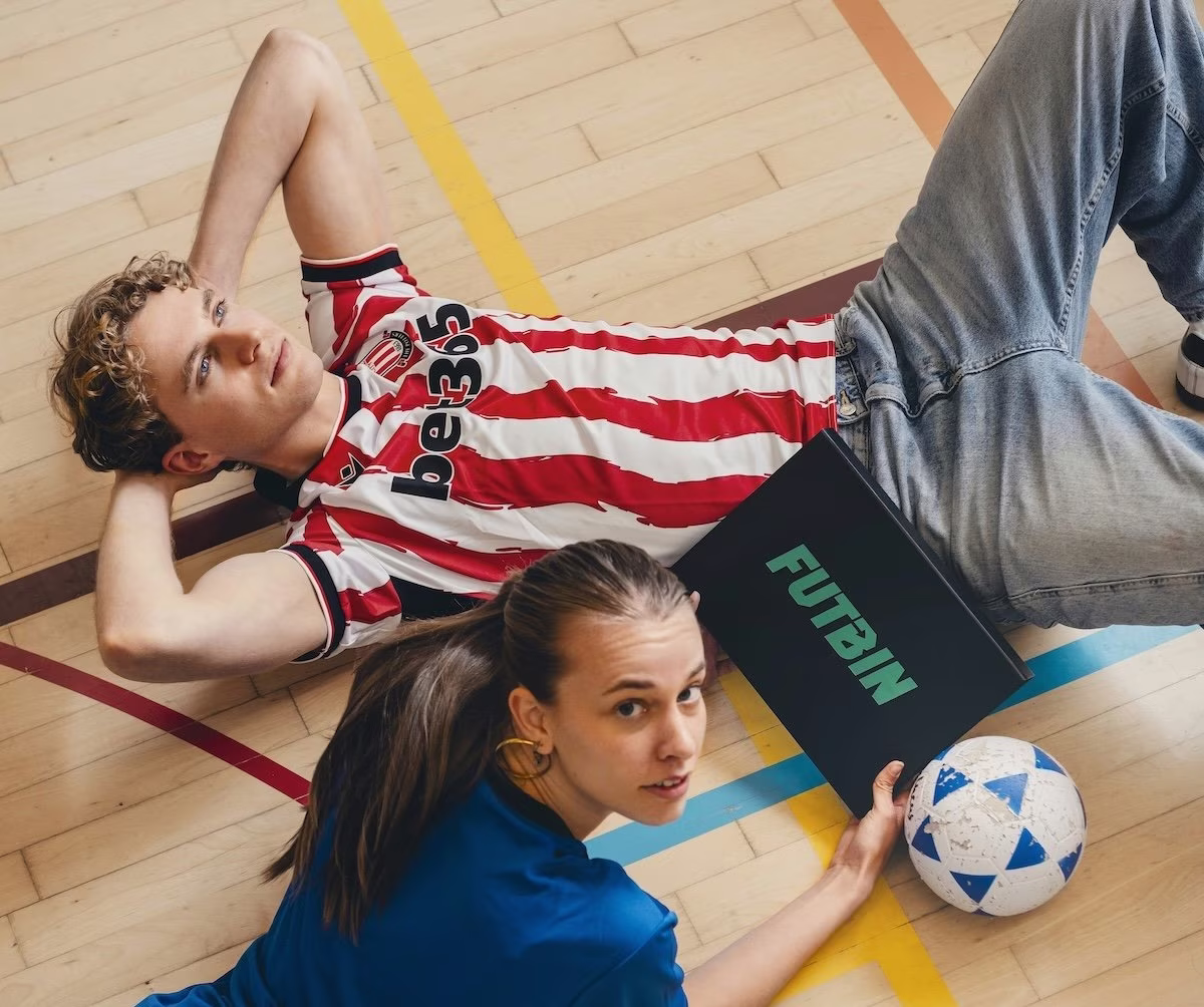 Two fans on a gym floor with a FUTBIN box and football